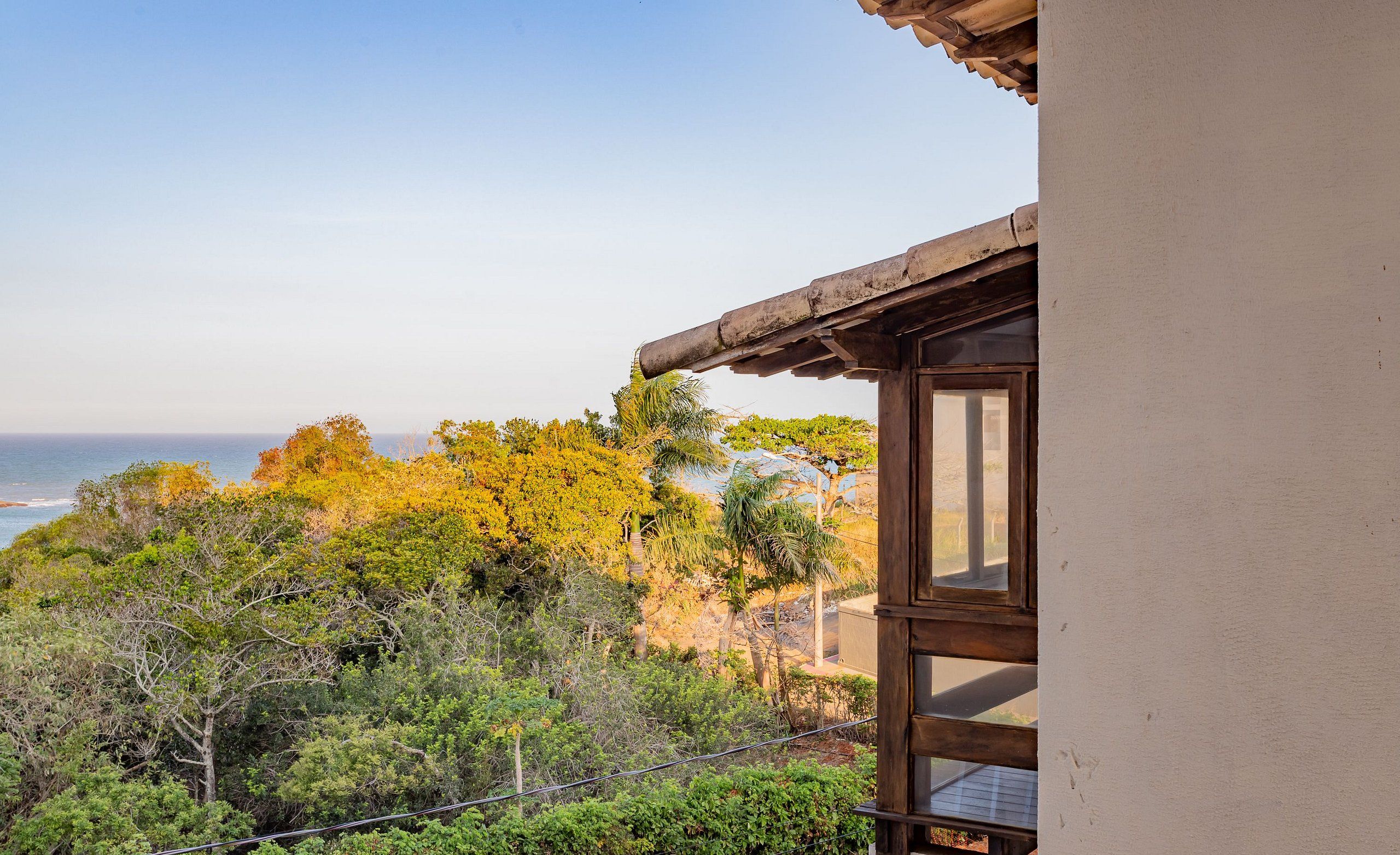 A coastal property with a balcony overlooking the sea, surrounded by dense foliage.