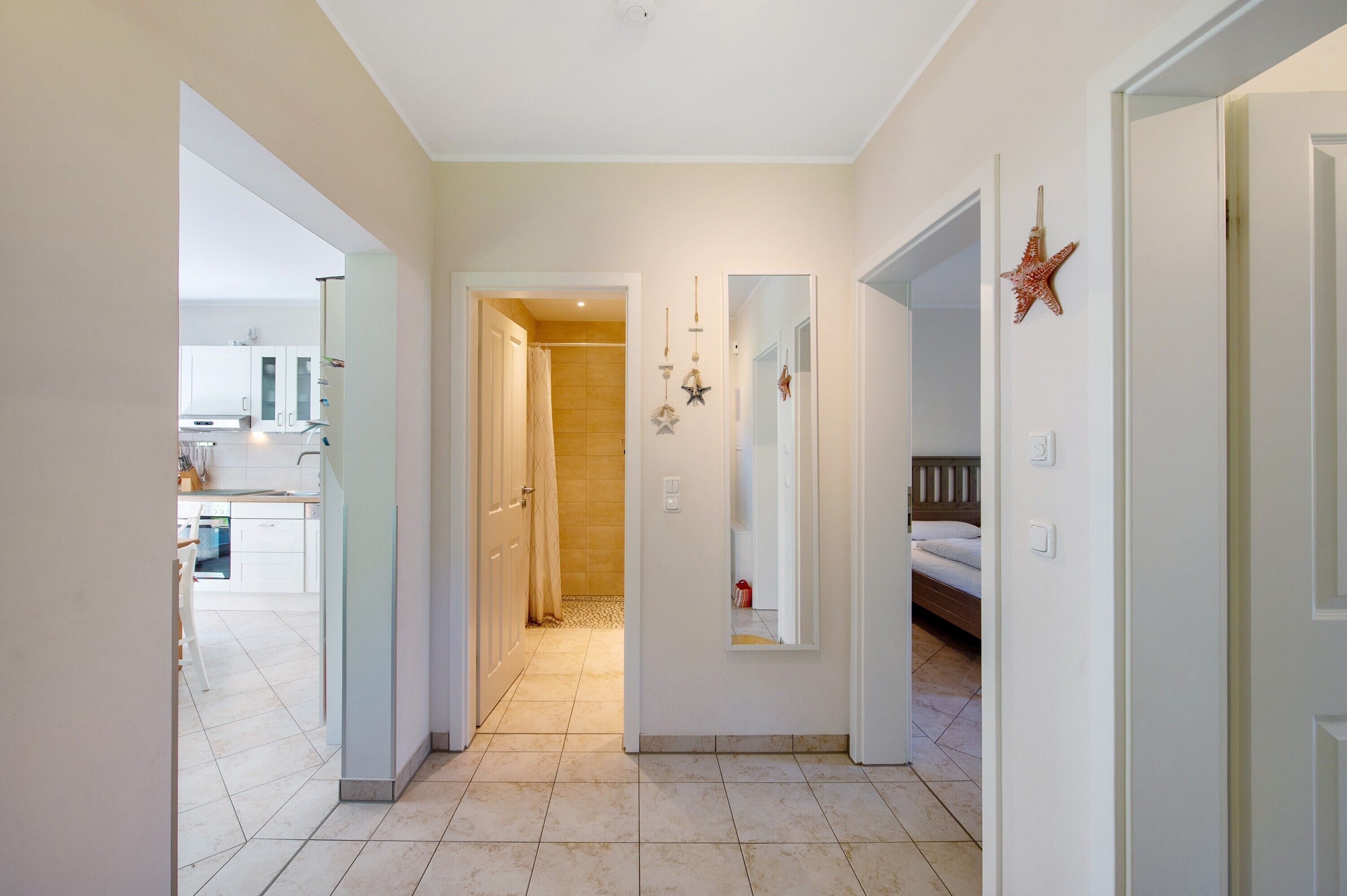 Un couloir avec une cuisine en arrière-plan, un miroir et une décoration en forme d’étoile sur le mur.