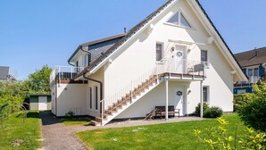 Una casa de dos pisos con una escalera que lleva a un balcón, una puerta principal y un pequeño jardín.