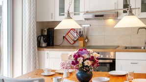 Una mesa de comedor con un florero, sillas blancas y una cocina al fondo.