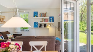 Una sala de estar acogedora con un sofá, una mesa de comedor con un florero y estanterías con libros y objetos decorativos.