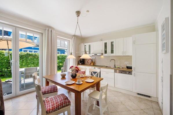 Une cuisine moderne avec des meubles blancs, une table à manger avec des chaises et une vue sur la verdure à l’extérieur.
