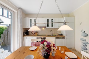 Une cuisine moderne avec des meubles blancs, une table à manger en bois et un grand vase rempli de fleurs.