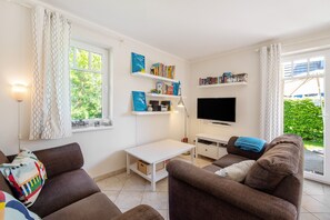 Un salon avec un canapé, un téléviseur, des étagères et une fenêtre avec des rideaux.