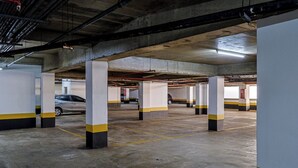An underground parking garage with concrete pillars, yellow and black striped columns, and a car parked in the distance. - Barra da Tijuca Vista Mar Lazer e Garagem (Rio de Janeiro)