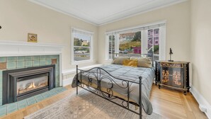 A bedroom with a fireplace, a bed with a headboard, a nightstand, and a dresser.