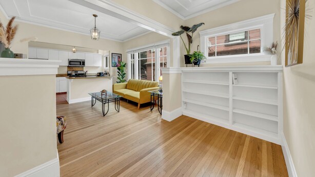 A spacious living area with a wooden floor, a yellow sofa, a dining table, and a kitchen in the background.