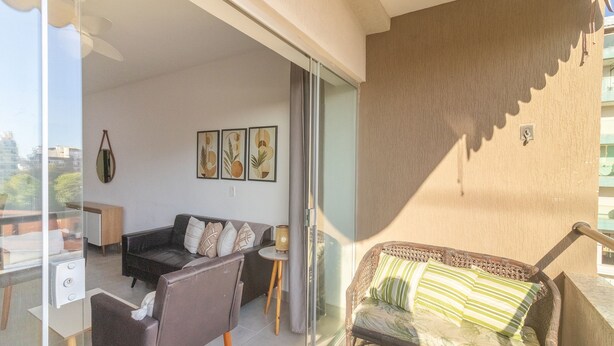 A living room with a sofa, a chair, a small table, and a glass door leading to an outdoor area. - Apt w/ Balcony 650m From Beach, Cabo Frio Cvy0306 (Cabo Frio)