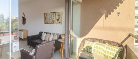 Una sala de estar con un sofá, una silla, una mesita y un ventanal de vidrio que da a un espacio al aire libre.