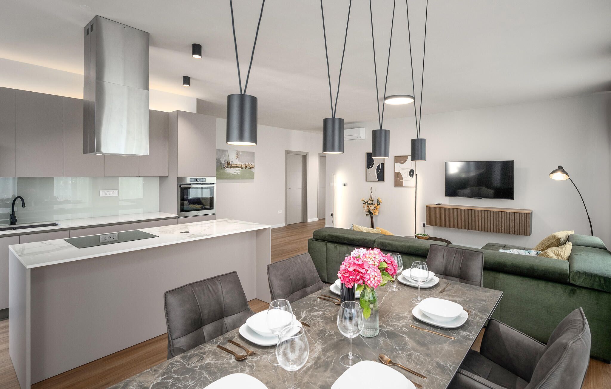 Una cucina moderna con un'isola centrale, una zona pranzo con tavolo in marmo e un soggiorno con divano verde.