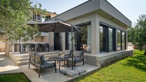 Une terrasse extérieure moderne, dotée d’un ensemble de mobilier de jardin, d’un grand parasol et offrant une vue sur les environs.
