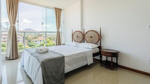 A hotel room with a large bed, a small round table, and a view of the cityscape through large windows.
