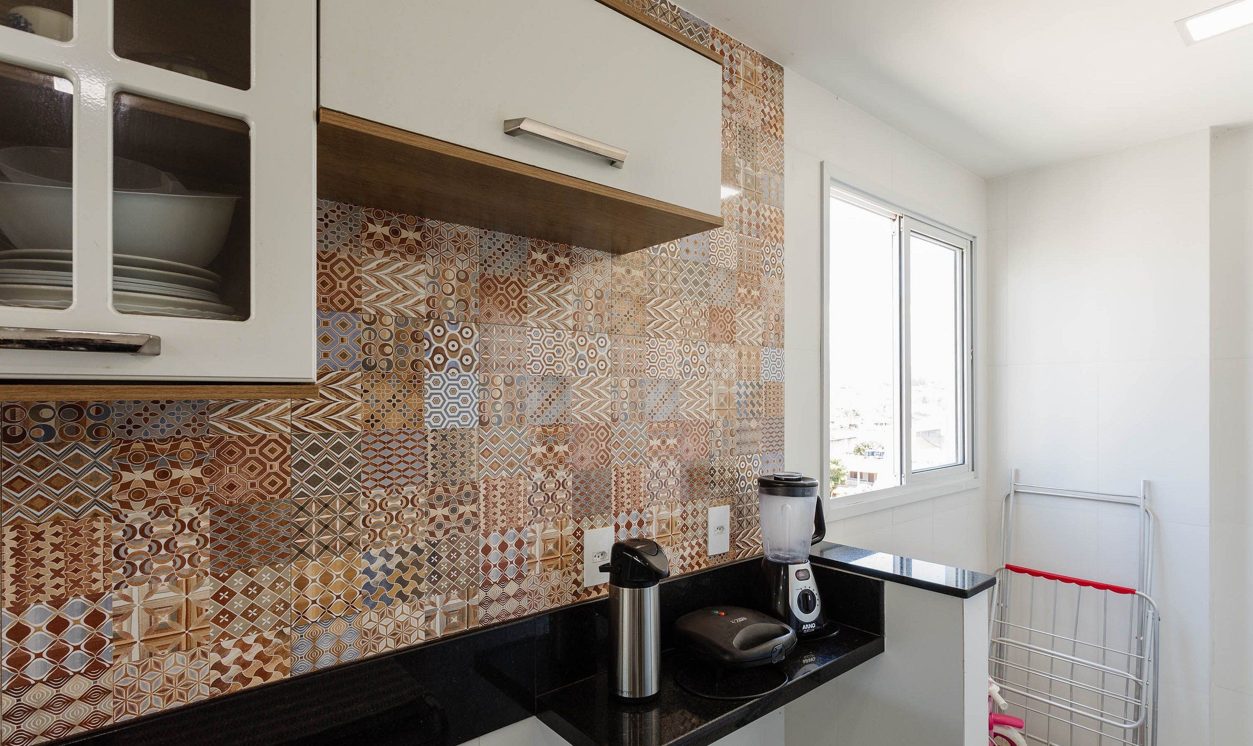 Una cocina con baldosas estampadas, un ventanal y una encimera con un hervidor y una licuadora.