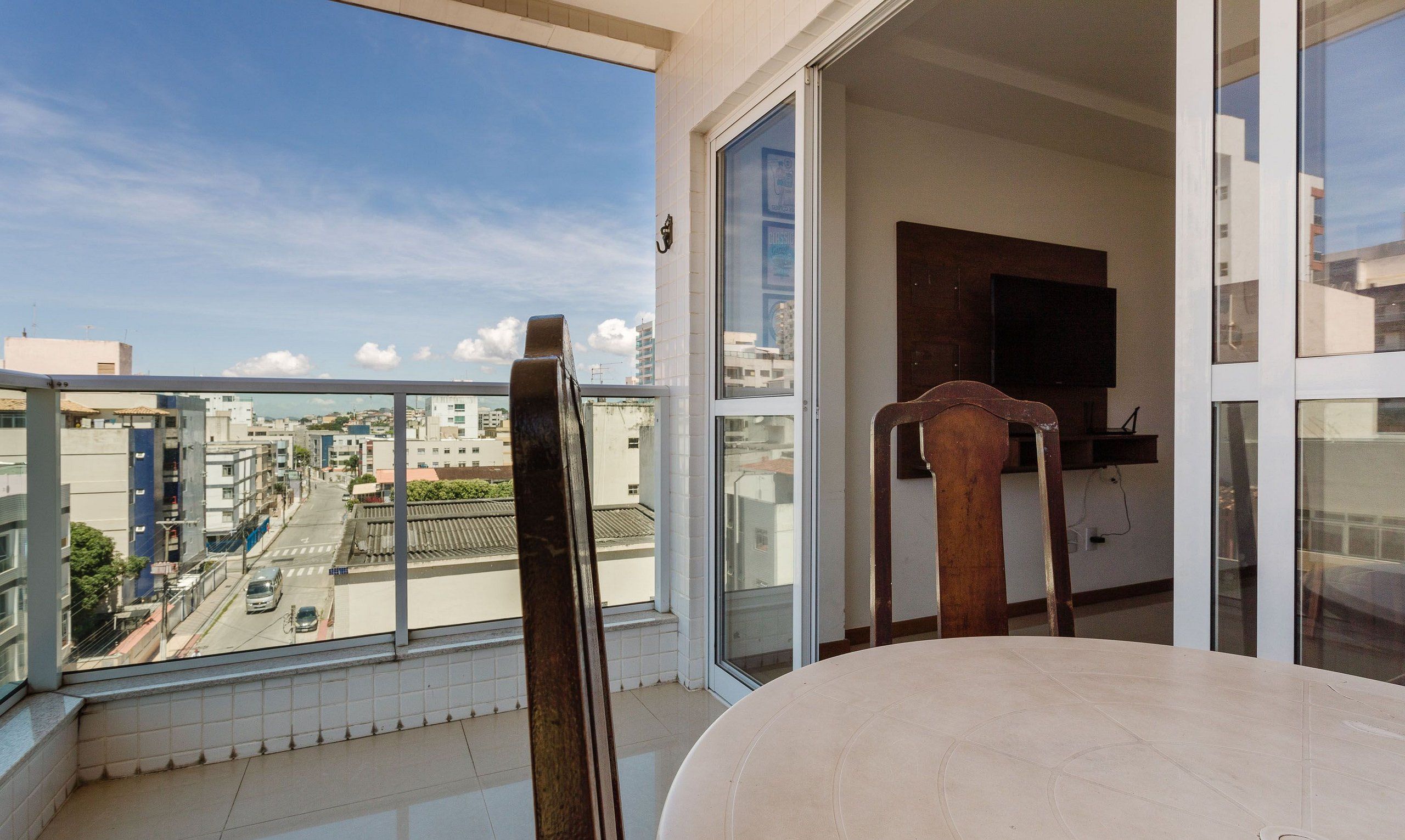A balcony with a view of a city street, a wooden chair, and a table.