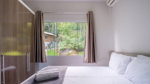 Une chambre à coucher avec un lit, une fenêtre avec des rideaux et une vue sur une maison et des arbres.