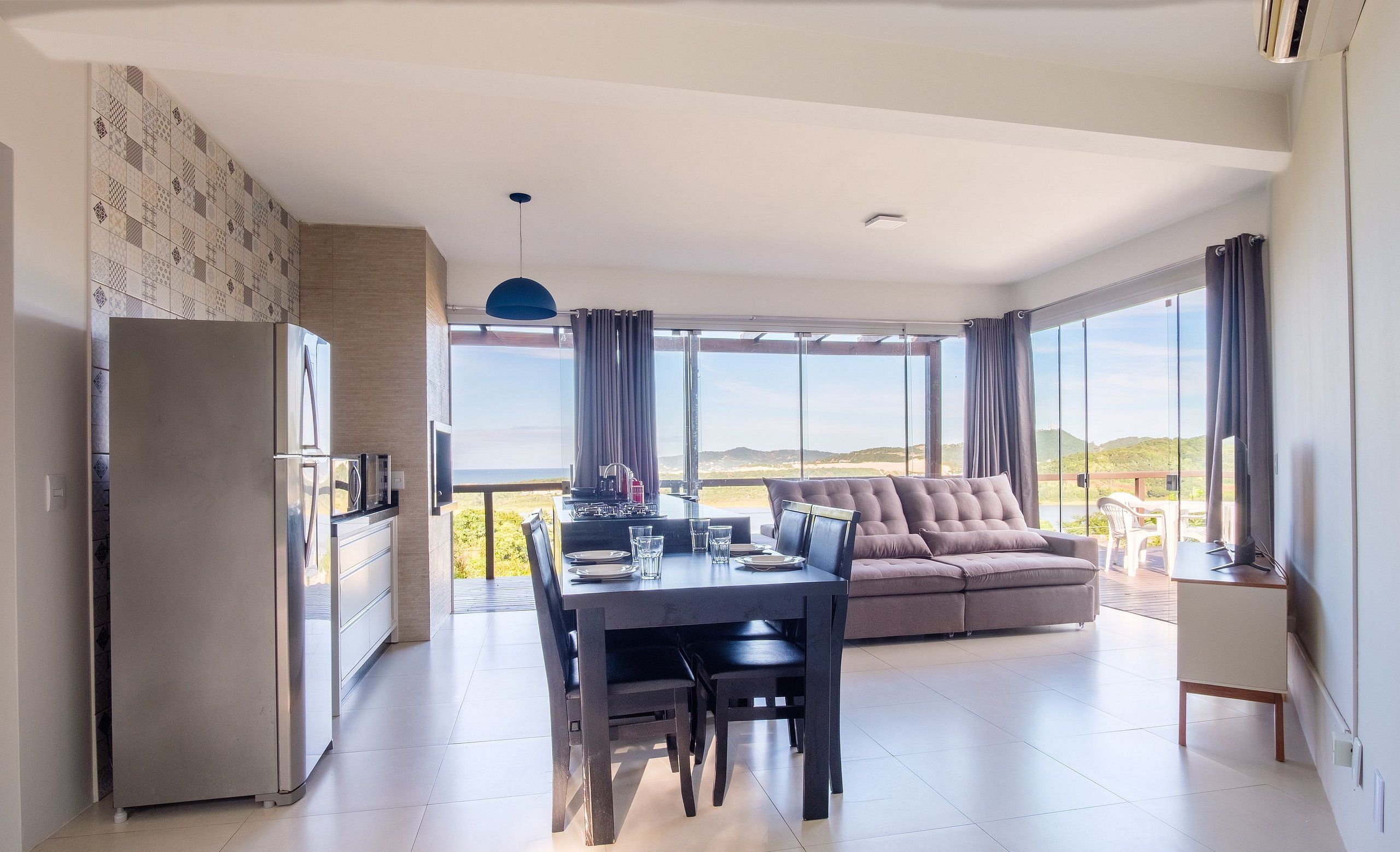 Uma sala de estar moderna com área de jantar, sofá e uma janela ampla com vista para o exterior.