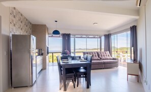 A modern living room with a dining area, a sofa, and a large window offering a view of the outdoors. - House With Lagoon View and Barbecue Ctm0000 (Garopaba)
