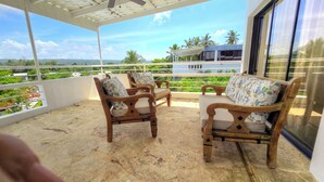 A covered outdoor seating area with wooden chairs and a table, overlooking a lush landscape with palm trees and a distant mountain range. - 3 BR Penthouse Center Cabarete (Cabarete)