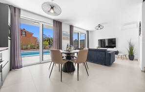 Un salon moderne avec un coin repas, un téléviseur et une vue sur la piscine.