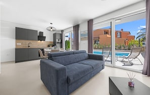 Ein modernes Wohnzimmer mit grauem Sofa, ein Essbereich mit Tisch und Stühlen, eine Küche mit dunklen Schränken und ein Poolbereich mit Liegestühlen.
