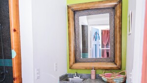 A bathroom with a green wall, a wooden-framed mirror, a sink with a soap dispenser, and a patterned curtain.