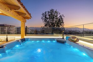 En uppvärmd bubbelpool på taket, med en pergola av trä, ett glasräcke och utsikt över staden och bergen.