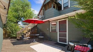 Een terras met een tafel en stoelen, een rode parasol en een trap naar de tweede verdieping.