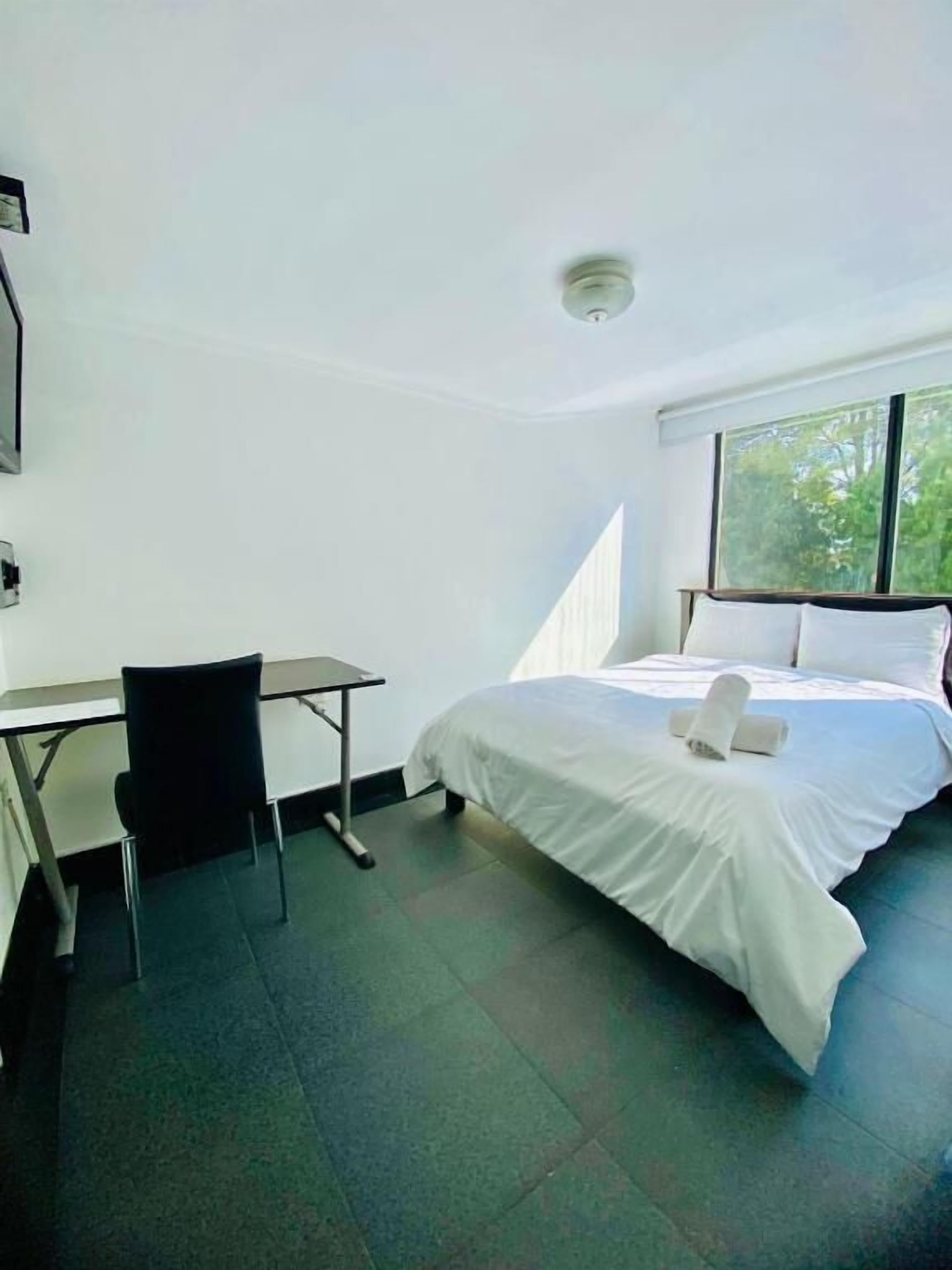 Una habitación de hotel con cama, escritorio, silla y ventana.