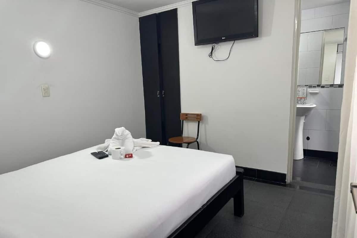 Ein Hotelzimmer mit Bett, Wandfernseher, Sessel und einem durchgegangenen Tür erkennbaren Badezimmer.