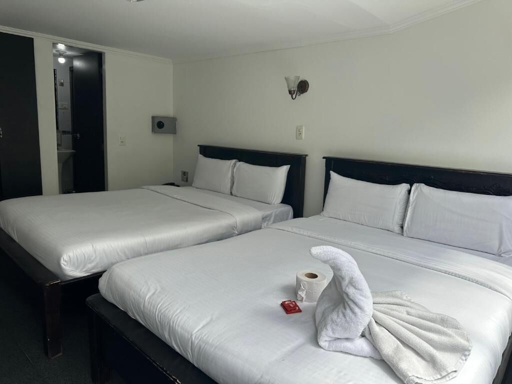 Two single beds with white linens, a towel, and a roll of toilet paper on one bed.