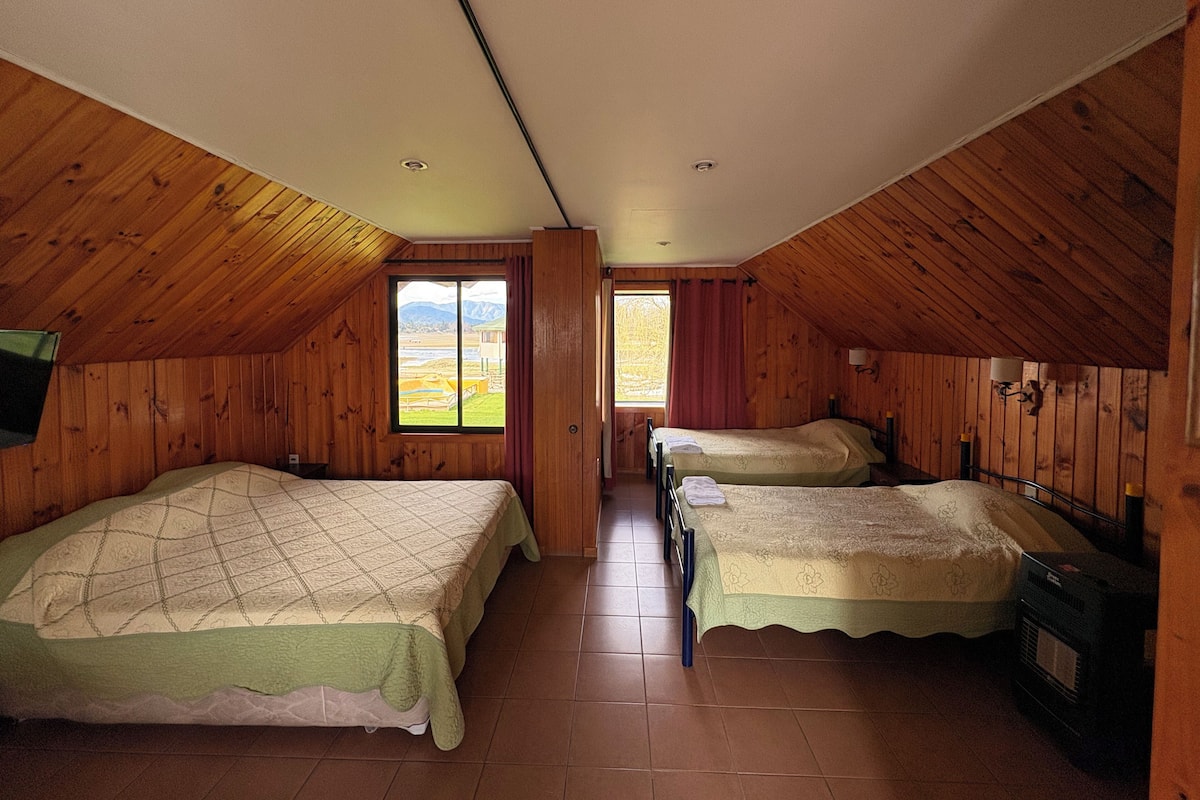 A room with two beds, wooden walls, a window with a view, and a tiled floor.