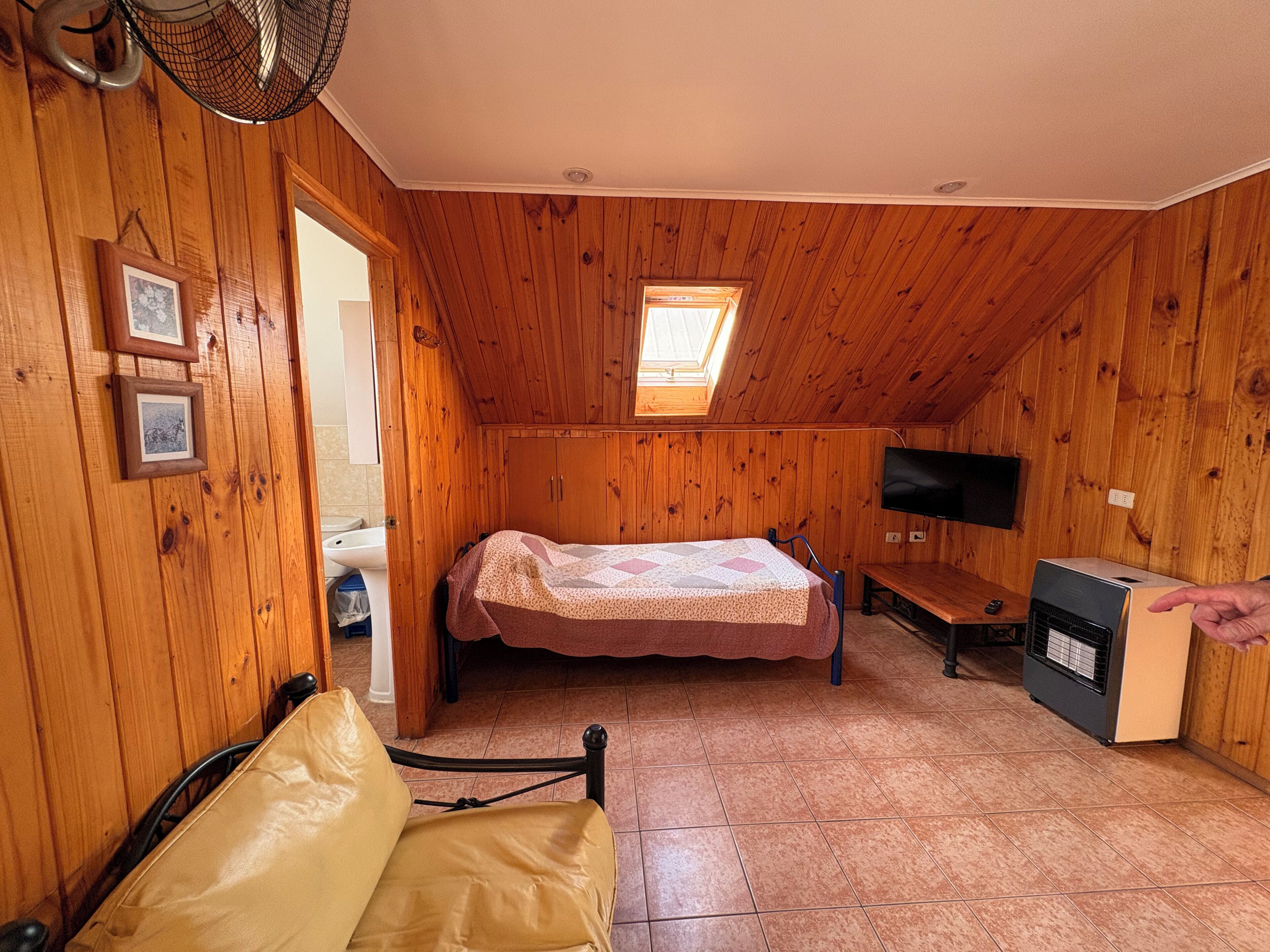 Un dormitorio acogedor en el ático con paredes de madera, una cama, un televisor y un calentador.