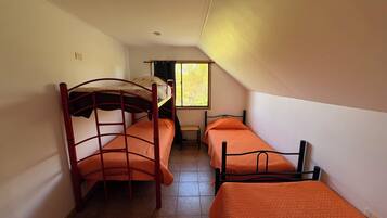 Un dormitorio con dos literas y una cama individual, una ventana con vistas a árboles y suelo de baldosas.