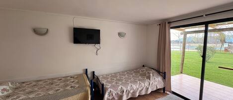 A room with two beds, a television mounted on the wall, and a sliding glass door leading to an outdoor area.