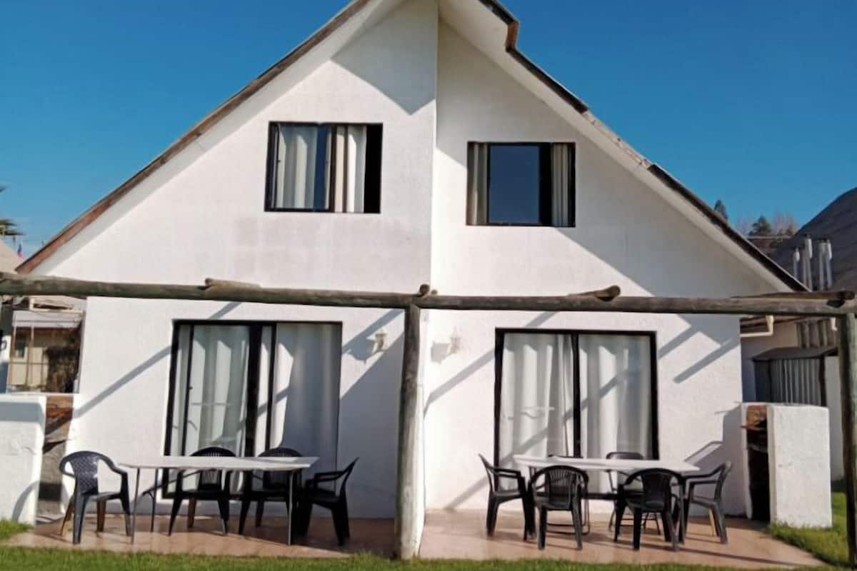 A two-story house with a sloped roof, large windows, and a covered patio area with outdoor furniture.