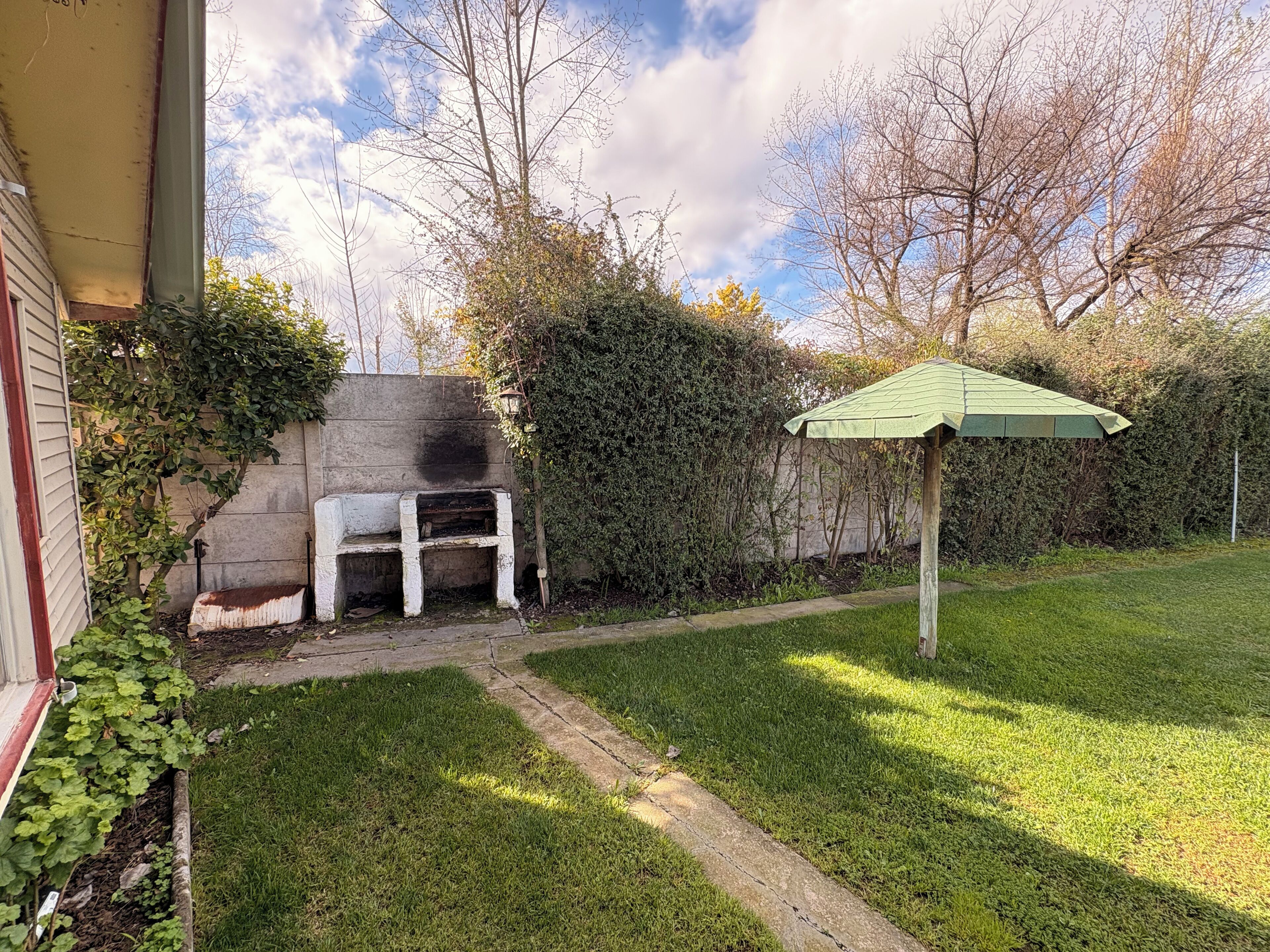 A backyard with a barbecue grill, a small wooden bench, and a green umbrella.