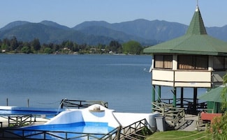 Vista de un lago con una pequeña torre de vigilancia, barcos y montañas al fondo.
