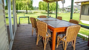 A covered outdoor dining area with a wooden table and wicker chairs, overlooking a grassy landscape with trees and a distant building. - Cabañas Villa Alejandra (Las Cabras)