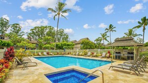 Una piscina con jacuzzi, rodeada de tumbonas y palmeras.