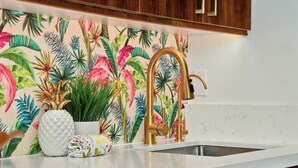 Una cocina con encimera blanca, grifo dorado y decoración temática tropical.