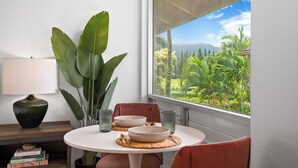Un comedor con una mesa, sillas, una lámpara y vistas a un jardín exuberante a través de una ventana.