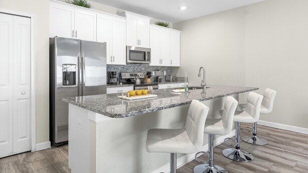 A modern kitchen with white cabinets, stainless steel appliances, a granite countertop, and bar stools. - Champions Gate Resort Home with Pool (Four Corners)