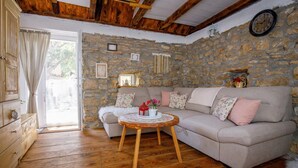 A cozy living room with a stone wall, wooden ceiling beams, a beige sofa, and a round wooden coffee table.