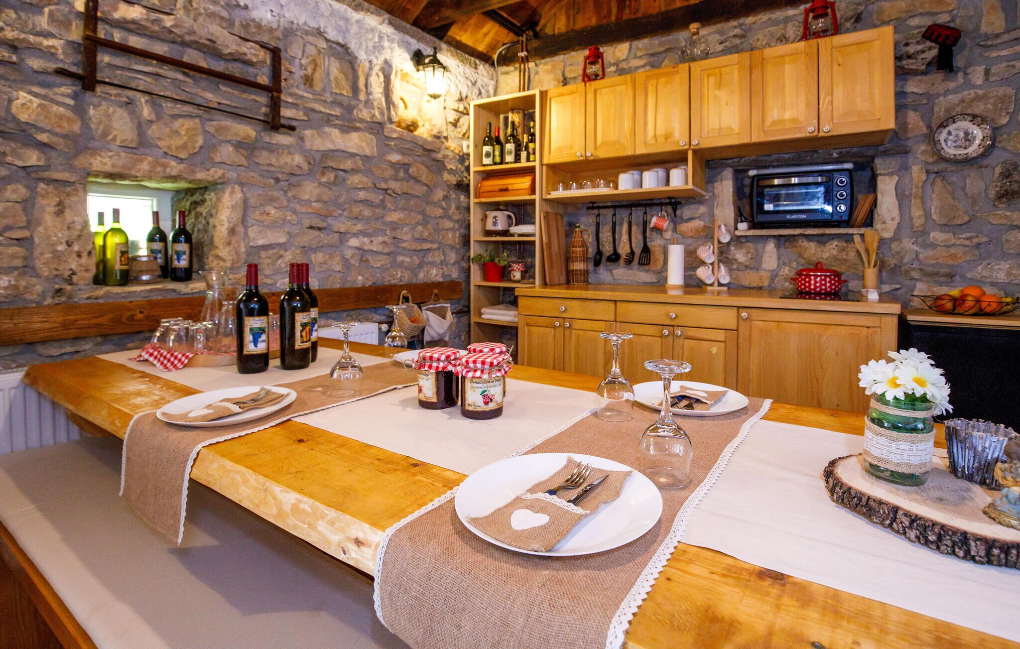 Comedor rústico con paredes de piedra, muebles de madera y una zona de cocina con microondas y diversos utensilios.
