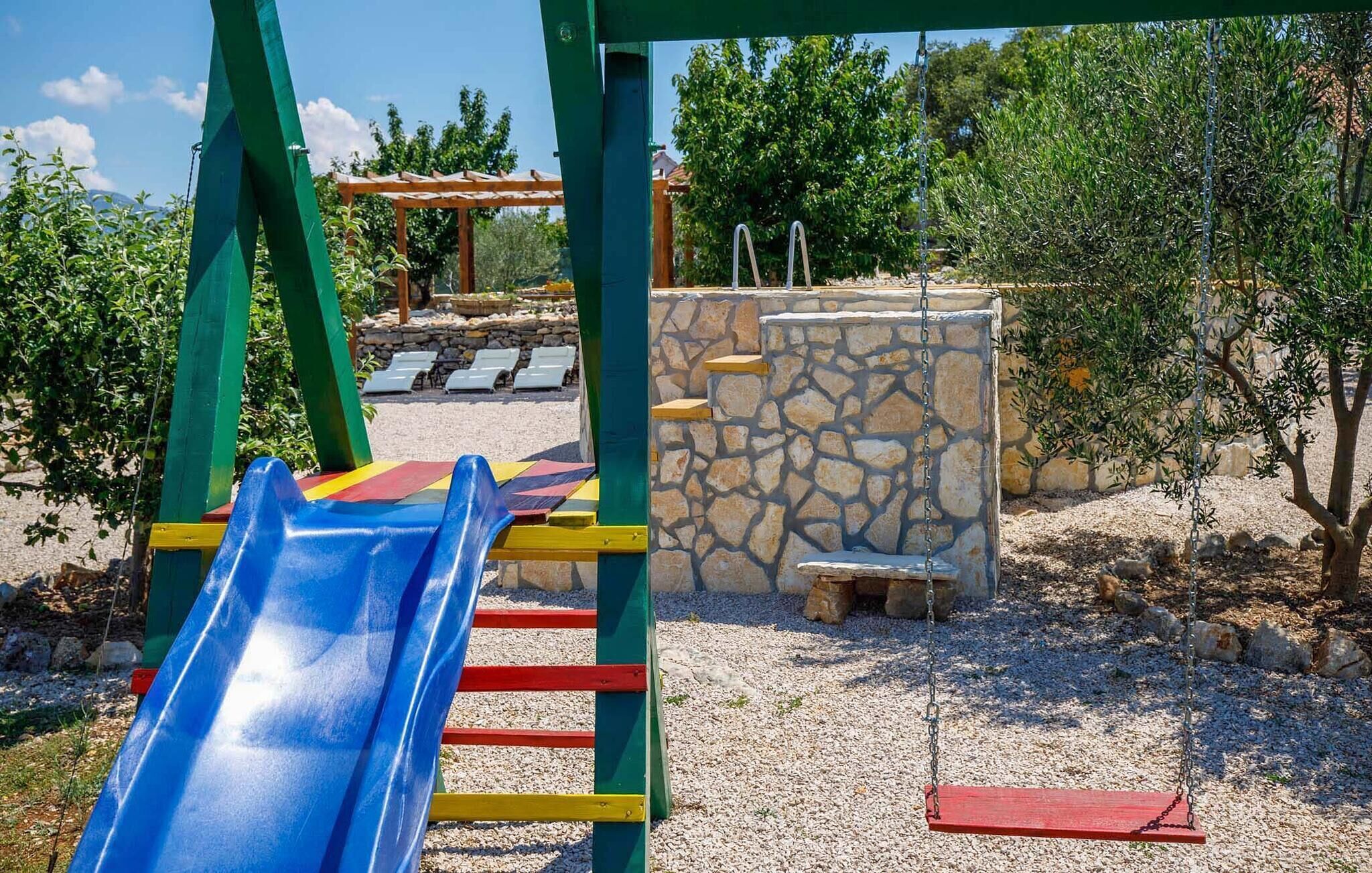 Une aire de jeux avec un toboggan bleu, des marches rouges et jaunes, et un mur en pierre.