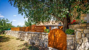 A stone wall with a wooden gate, a stone building with a tiled roof, and a tree with green leaves.