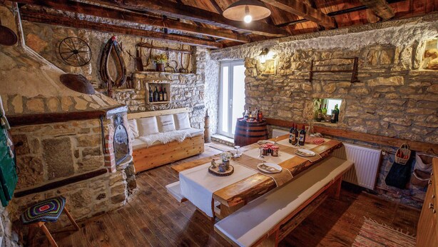 A rustic stone-walled room with a wooden bench, a stone fireplace, and a wooden dining table set for a meal.