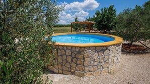 A swimming pool with a stone wall, surrounded by olive trees and a pergola.