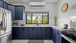 Una cucina moderna con mobili blu scuro, un frigorifero in acciaio inossidabile, un forno integrato e un'ampia finestra che si affaccia sul verde.