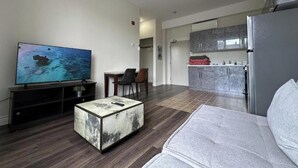 A modern living room with a flat-screen TV, a coffee table, and a sofa. - Deluxe One-Bedroom Apartment with City View (Oshawa)
